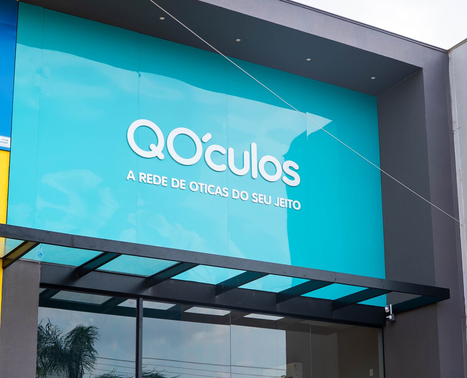 Fachada turquesa da QÓculos Sinop com o letreiro A rede de óticas do seu jeito